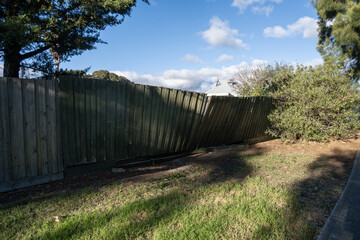 Fototapeta premium Leaning weathered timber paling fence or damaged wooden fencing in suburban Australia. Aging residential boundary fence. Concept of property maintenance, decay, and home improvement