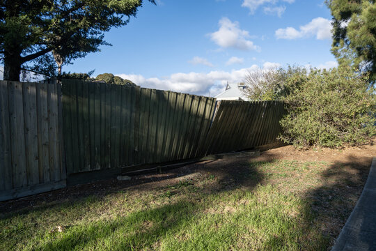 Leaning weathered timber paling fence or damaged wooden fencing in suburban Australia. Aging residential boundary fence. Concept of property maintenance, decay, and home improvement
