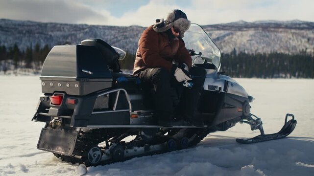 Ice fishing from a snowmobile on open frozen ice, surrounded by snow and distant winter scenery. Great for cold weather, wilderness, adventure and outdoor content.