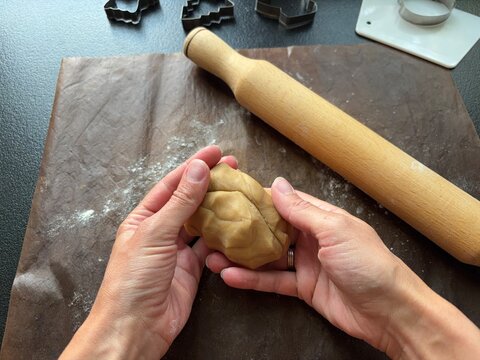 hands holding a ball of cookie dough with a rolling pin and cutters on a baking mat