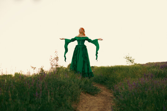 Faity tale silhouette of woman hands raised to twhite sky, green grass waving vintage victorian dress old style medieval clothing renaissance wide sleeves. Mystery person, sexy gothic elf girl praying
