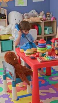 Boy playing with toy phone and stacking rings at red table inside a building playroom; playfulness imagination.