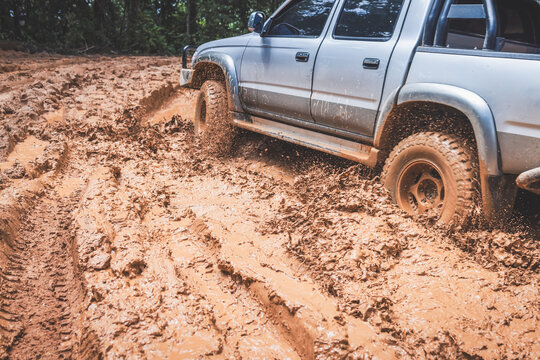 Powerful offroad wheels pushing through flooded mud trails, throwing water and mud into the air. 4x4 truck, mud tires, wheel spin, traction, overlanding, extreme off-road driving.