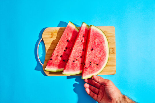 Hand reaching for a watermelon slice on a blue background