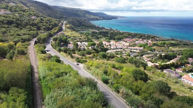 Costa degli Dei, Calabria, Italy. Aerial drone footage of the Tyrrhenian Sea coastline with seaside village, coastal road, railway line and green hills between Briatico and Tropea.