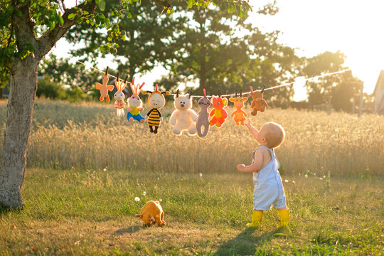 The baby reaches for the toys hanging on the rope in the garden at sunset.
