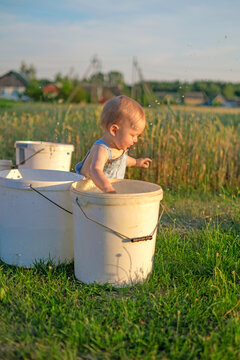 A small child splashing in a bucket of water in the garden. Children's pranks.