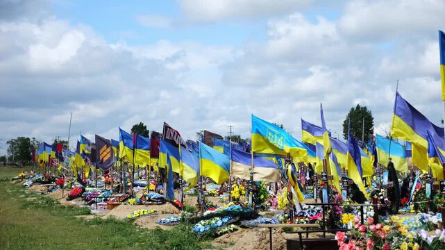 View from window of moving automobile on large military cemetery in Kharkiv with countless graves marked by Ukrainian flags. The site commemorates soldiers who died during russian invasion in Ukraine