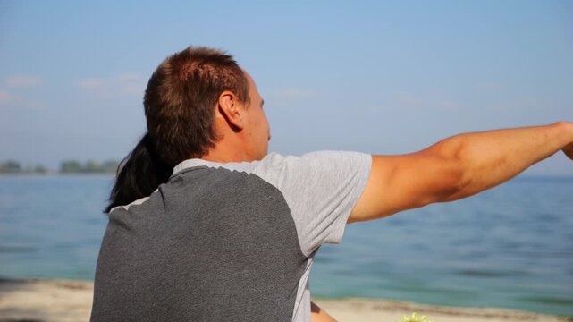 Happy pair hugs during sitting on wooden log on beach. Romantic couple admiring sea landscape at sunny day. Lovers spending time together at resort. Concept of summer vacation or holiday. Slow mo
