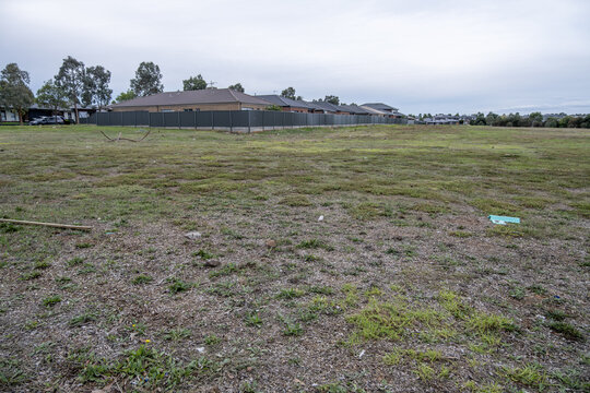 Vacant residential land with dry patchy grass beside established homes in Tarneit Melbourne Australia. Undeveloped suburban block. Land development, housing supply, and urban growth