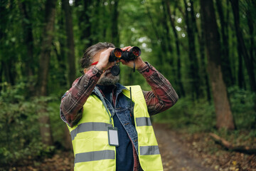 Naklejka premium Professional binoculars in hands. Senior forest ecologist is working in the woods. In the uniform