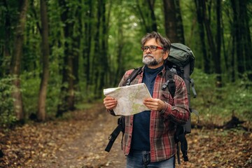 Obraz premium Paper map is in hands. Hiking experience, senior man is in the forest at daytime