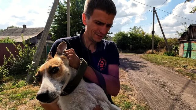 Male volunteer carrying in hands dog to evacuate from frontline city. Russian attacks endanger lives daily both human and animal in ukrainian territory. The scene shows need to protect innocent