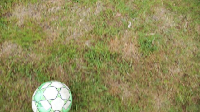 Male feet of professional footballer kicks ball during jogs at meadow on summer day. Legs of sportsman shows tricks with ball while running at green field. Young man training at stadium. POV