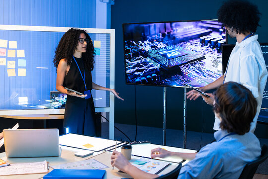 Female developer stand present artificial intelligence processing unit layout on screen during team brainstorm conference at tech startup office