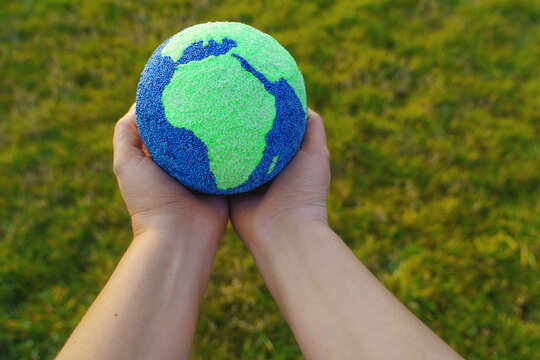Authentic image featuring real people. Little hands tenderly hold a small globe, symbolizing care for the planet and a hopeful future, with soft light and a blue background