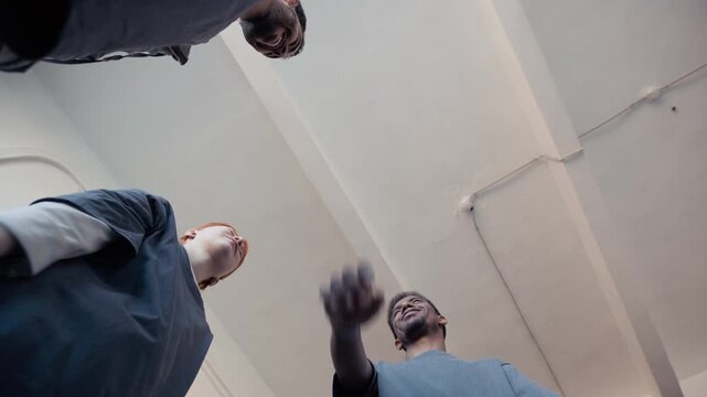 Diverse young adult volunteers stacking hands in huddle, low angle slow motion shot. Ideal for non-profit campaigns, community support ads, and corporate social responsibility videos