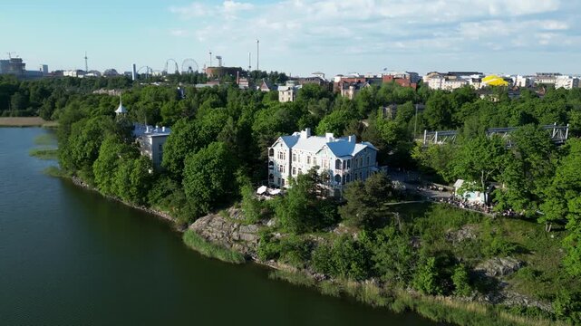 Aerial drone view of Art Cafe Terrace located by T&ouml;&ouml;l&ouml;nlahti Bay in Helsinki, Finland. Beautiful urban waterfront scenery featuring the caf&eacute; terrace, surrounding nature, and Helsinki city landscape.