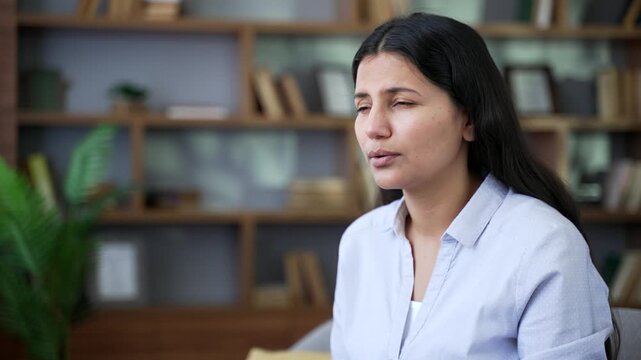 Allergic woman sneezes and wipes her nose with a handkerchief. Girl is sick with cold or flu. Unhealthy female suffering from seasonal allergies sitting on sofa in living room at home. Close up.