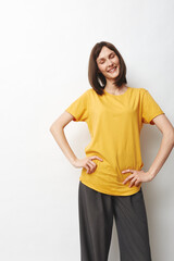 Obraz premium Young woman with shoulder length dark hair stands in a bright studio wearing a yellow tshirt and gray pants, smiling confidently.