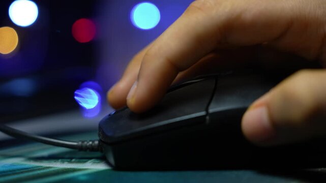 Close-up of a hand using a computer mouse on a desk with colorful blurred lights in the background