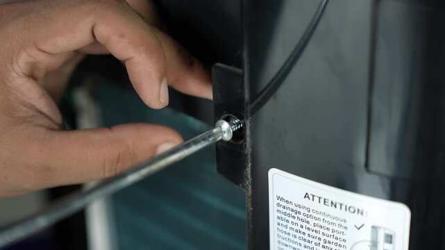 Hand using a screwdriver to tighten a screw on a black appliance panel, Hand tightening screw on appliance panel