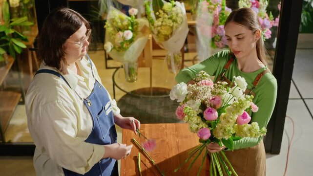 Young adult Caucasian florist training female colleague in flower shop, assembling fresh bouquet. Footage ideal for small business marketing, floristry workshops, and creative promotions