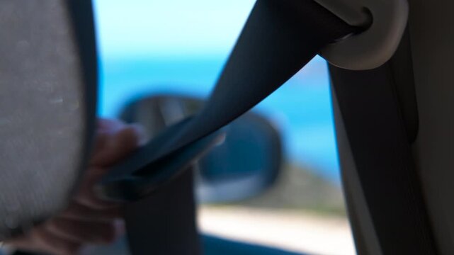 Person unbuckling car seat belt after parking. Close-up view from inside a vehicle of a person's hand unbuckling the safety belt after a journey, with the strap retracting into its holder