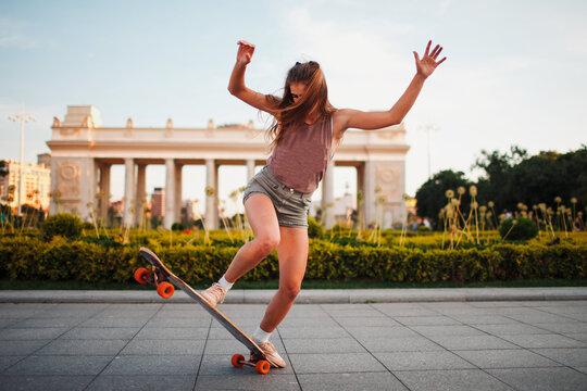 Young woman riding on the longboard skateboard in the park