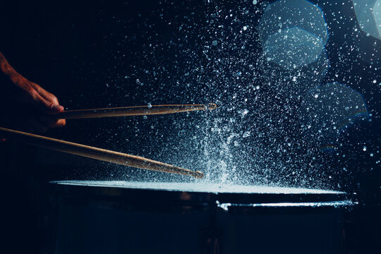 Drummer with drum sticks drumming beating rhythm on drum surface with splash water drops flying