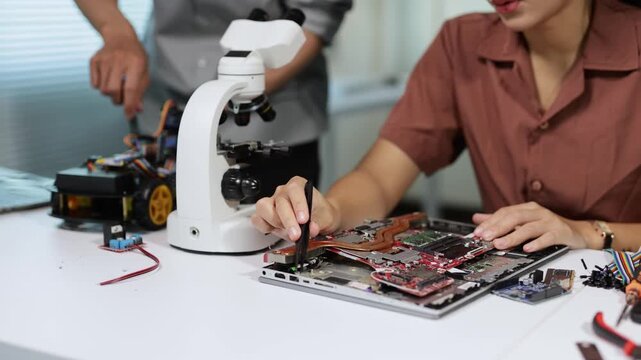 Female technician repairing computer motherboard with male engineer building a robot car in a modern technology laboratory