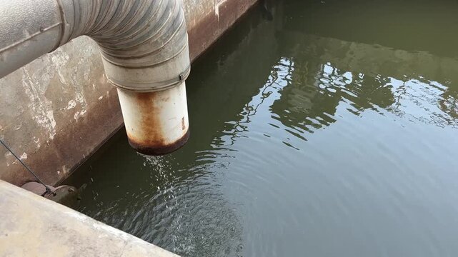 Water drips from rusted pipe into murky pond