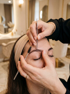 Professional beautician shaping eyebrows with tweezers in beauty salon