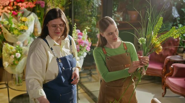 Two Caucasian young adult female florists collaborating on flower arrangement in floral shop. Perfect for small business marketing, entrepreneurship campaigns, and creative workshop promotions