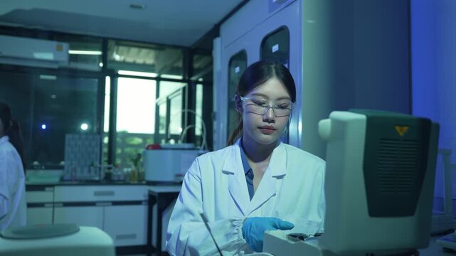 Asian scientist placing a biological sample into a thermal cycler machine for DNA amplification in a modern laboratory