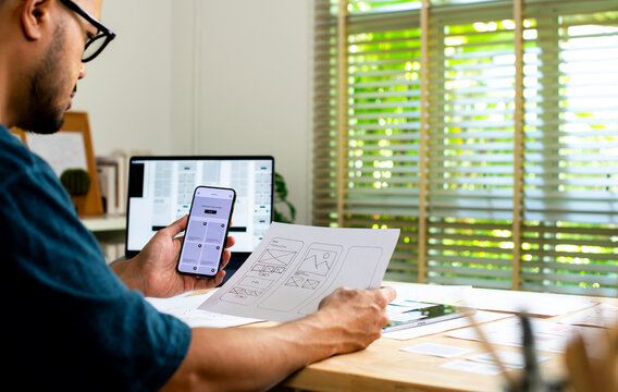 UX UI designer working on wireframes for a website and mobile app prototype, surrounded by sketches of user-flow and design tools, in concept of website and mobile application design concept.