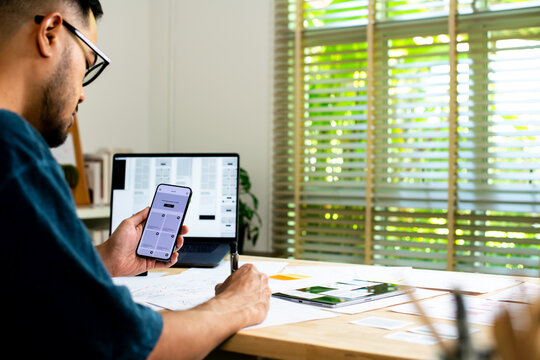 UX UI designer working on wireframes for a website and mobile app prototype, surrounded by sketches of user-flow and design tools, in concept of website and mobile application design concept.