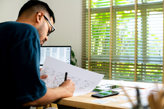 UX UI designer working on wireframes for a website and mobile app prototype, surrounded by sketches of user-flow and design tools, in concept of website and mobile application design concept.