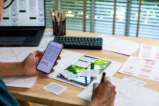 UX UI designer testing prototype on a phone, working on wireframes for a website and mobile app prototype, in concept of website and mobile application design concept.
