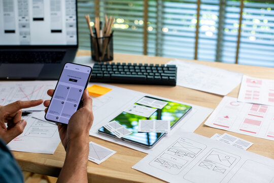 UX UI designer testing prototype on a phone, working on wireframes for a website and mobile app prototype, in concept of website and mobile application design concept.