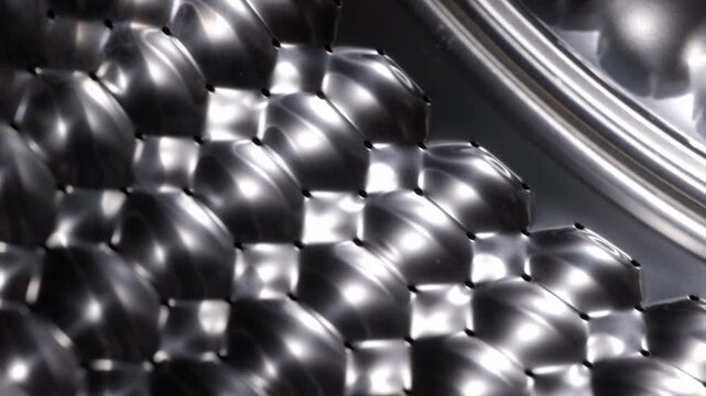 Stainless steel washing machine drum rotating. Empty and clean washing machine drum made of shiny stainless steel with a honeycomb pattern rotating, providing a detailed close-up view
