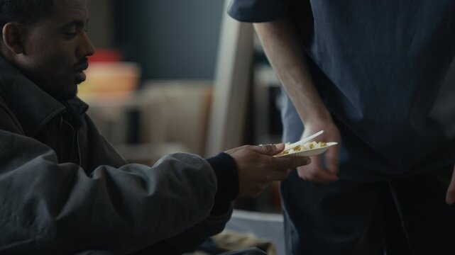 Black young adult man receiving food plate from Middle Eastern volunteer and having calm supportive conversation in shelter. Clip suitable for charity campaigns and social support promotions