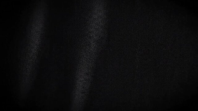Soft light movement across a dark black textured background with subtle grain and shadows