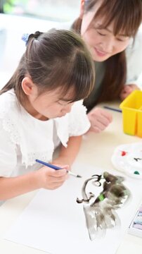 母親や先生に見守られながら美術や図工で水彩画を描く小学生位の女の子・創造力を育む親子の知育時間縦動画