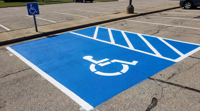 Accessible parking space for disabled driver in empty outdoor lot, blue painted asphalt with white wheelchair symbol and striped access zone
