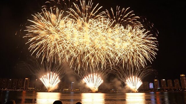 Spectacular golden fireworks display over urban waterfront city skyline at night.