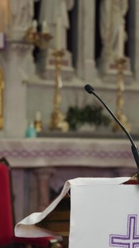 Preacher standing behind a pulpit with a microphone in a church, reading from a Bible to deliver a sermon, homily, or lead prayer.