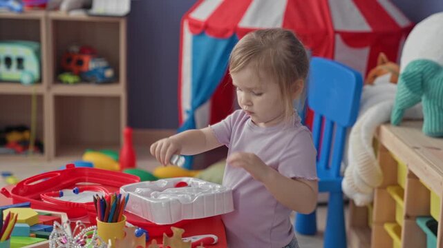 Toddler girl using hands to open a red plastic playset and sort colorful blocks in a daycare building; playful curiosity.
