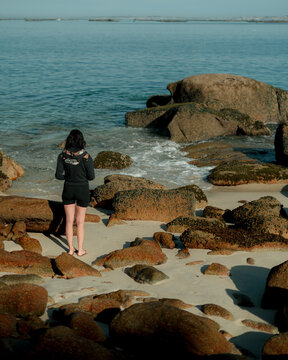 Woman Standing on Rocky Beach Looking Out to Sea &ndash; Peaceful Coastal Moment