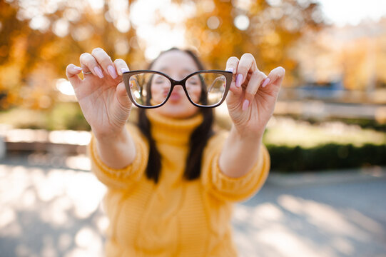Woman holding eye glasses in hands over autumn leaves close up. Healthcare.